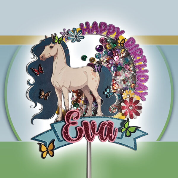 Close-up of the layered horse shaker cake topper highlighting its intricate paper layers, pink glitter lettering, and colorful confetti backdrop. The graceful horse, detailed butterflies, and flowers stand out against the transparent film filled with beads and sequins. Perfect for a little girl’s pony- or unicorn-themed birthday, this 5.5-inch-wide topper is supported by a clear acrylic stick.